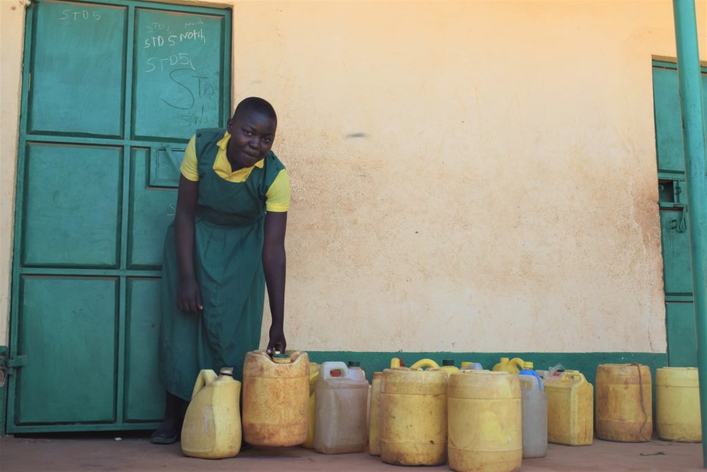 The Water Project : kenya19237-student-fetches-water-from-containers-in-front-of-classroom