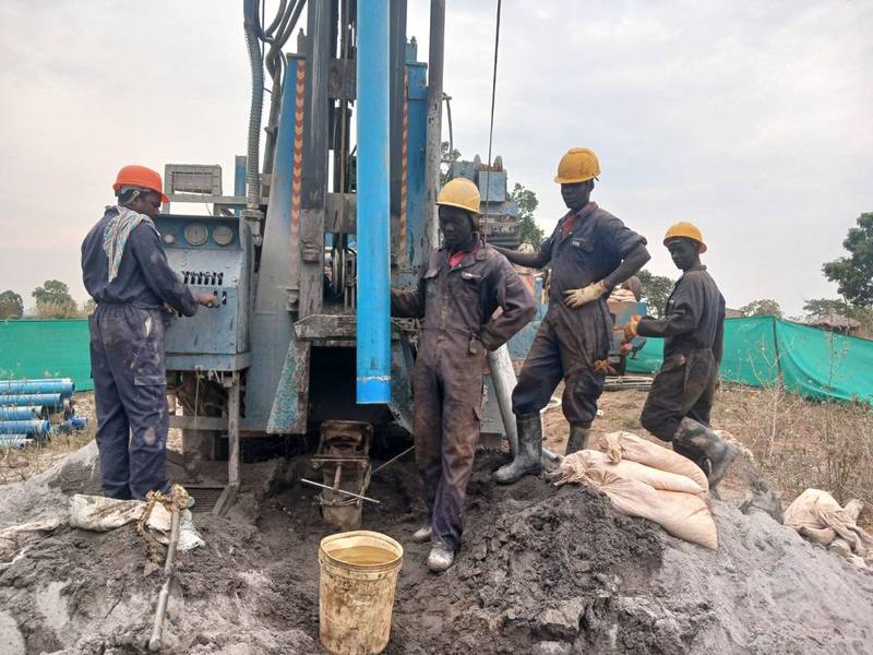 A local drilling crew in hard hats works the rig at a new borehole site.