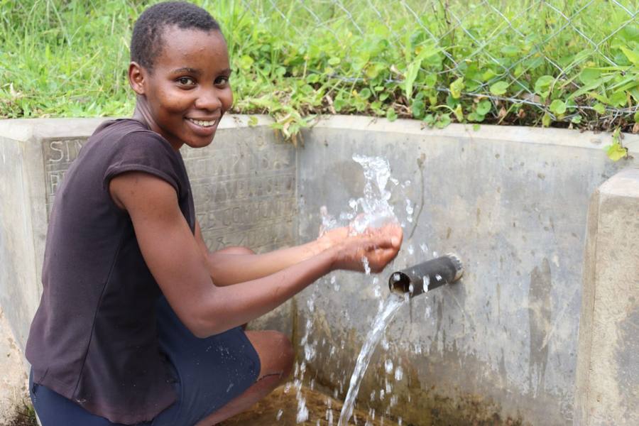 A smiling student washes her hands under clean running water.
