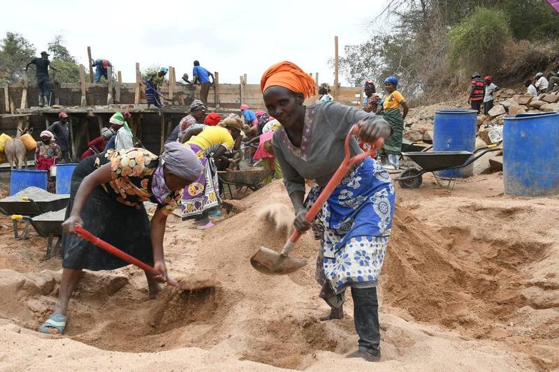 Community members dig sand and carry it by hand to build a sand dam.